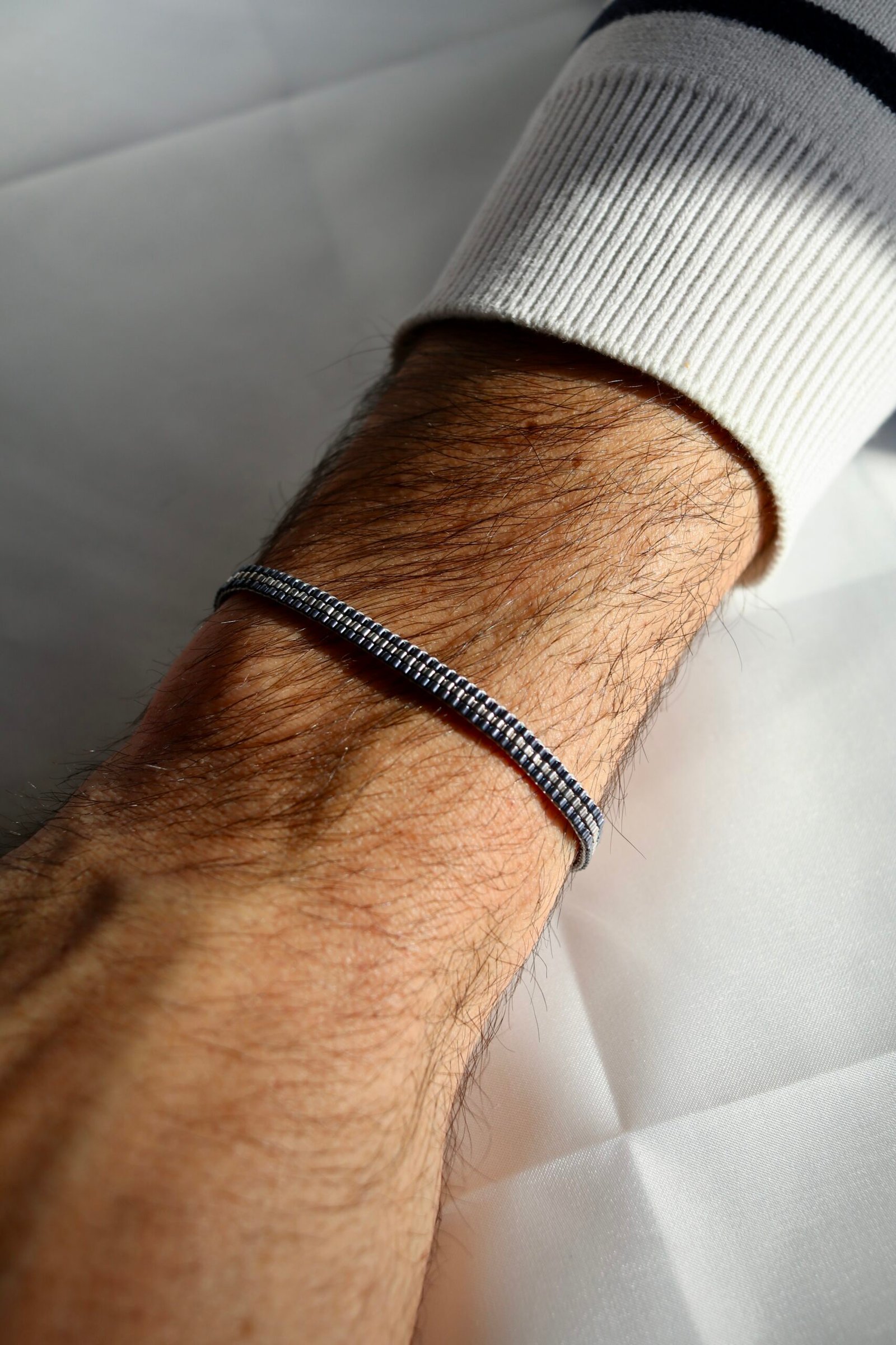 Un bracelet au caractère minéral et lumineux, mêlant un gris argenté palladium à un contour gunmetal bleu acier. Une création sobre, moderne et élégante, pensée comme un bijou intemporel pour homme.