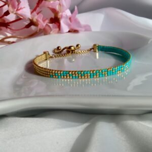 Lagune d’Or est un bracelet fin tissé à la main en perles Miyuki, mêlant bleu turquoise lumineux et or éclatant. Un bijou frais, solaire et élégant, inspiré par les eaux cristallines.