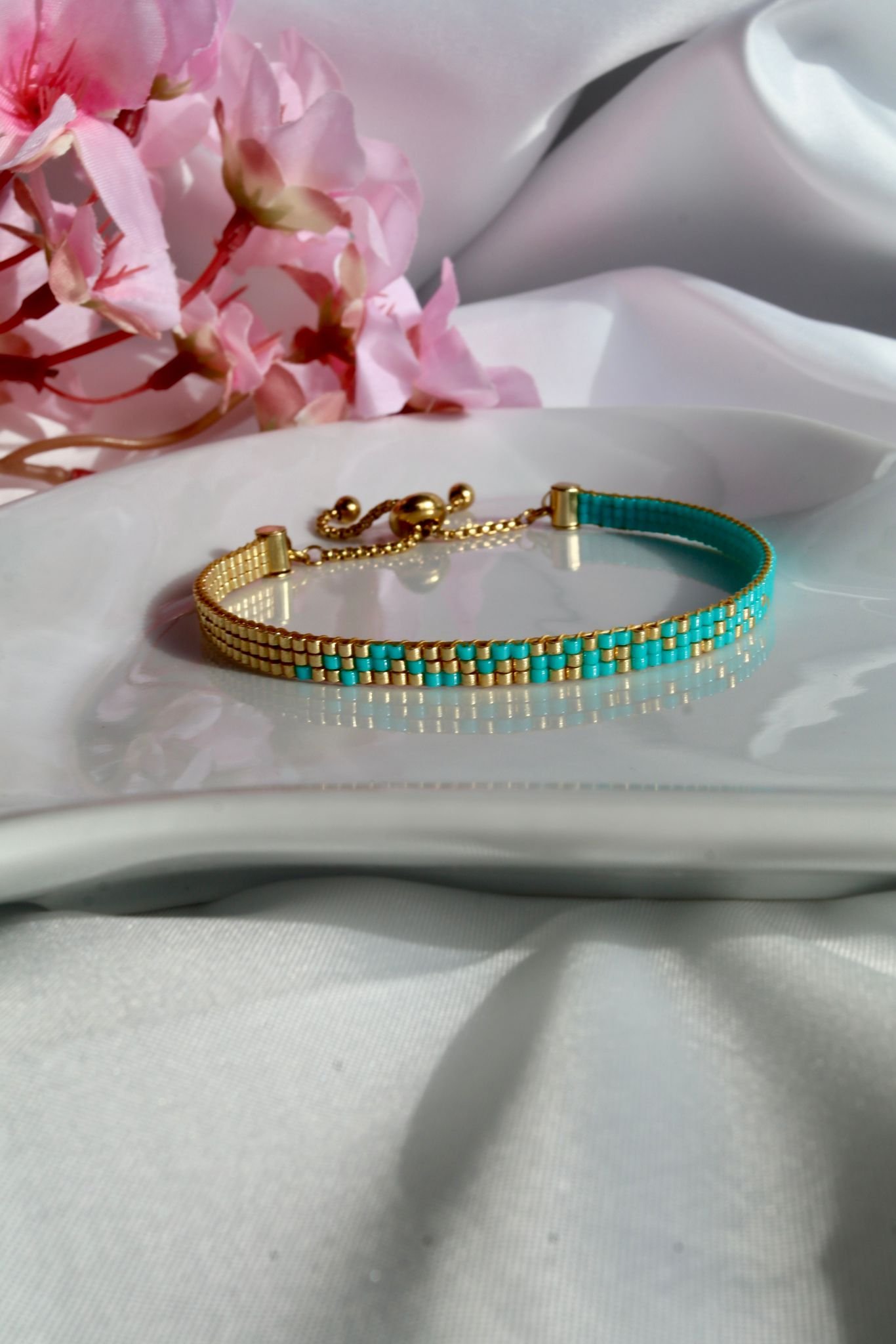 Lagune d’Or est un bracelet fin tissé à la main en perles Miyuki, mêlant bleu turquoise lumineux et or éclatant. Un bijou frais, solaire et élégant, inspiré par les eaux cristallines.