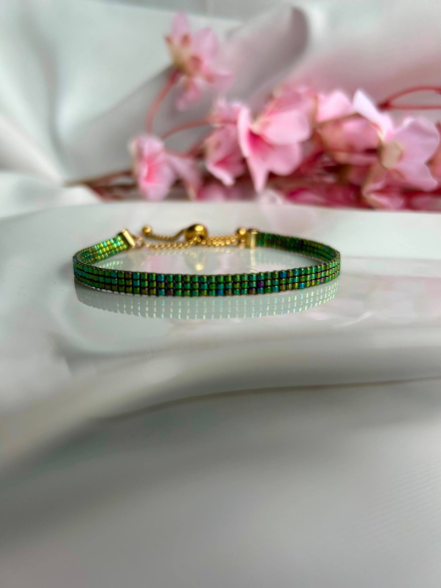 Bracelet fin tissé à la main en perles Miyuki. Inspiré des ailes délicates d'une libellule, Ailes d'Émeraude révèle de magnifiques reflets verts, turquoise et violets qui évoluent au gré de la lumière. Élégant, mystérieux et lumineux, il apporte une touche de nature et de magie à votre poignet.